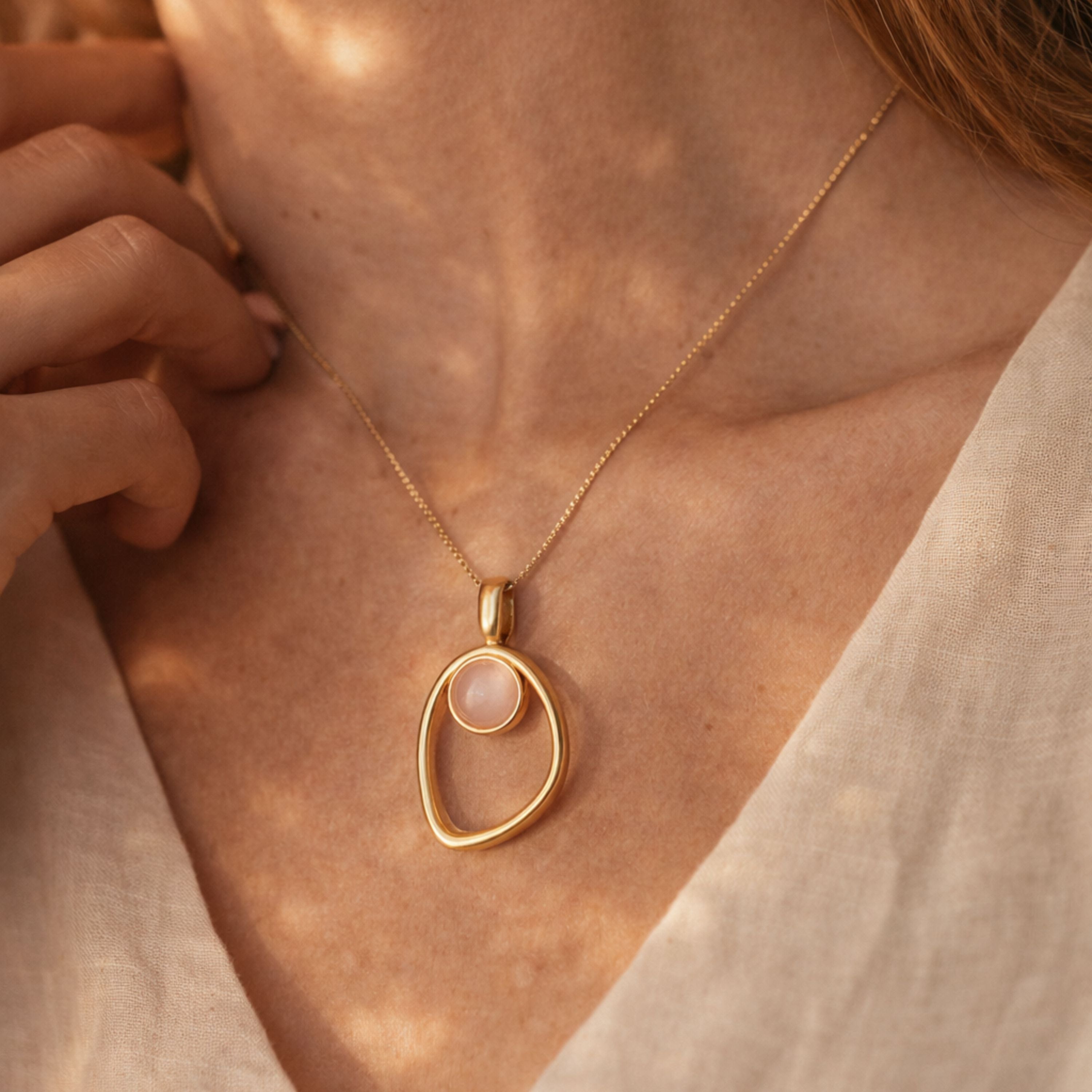 Gold necklace with a quartz rose pendant worn by a person, focusing on the jewelry.